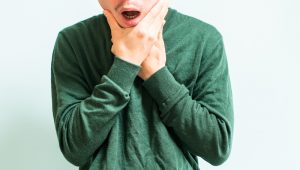 Man wearing a green shirt grasping his face due to TMJ pain