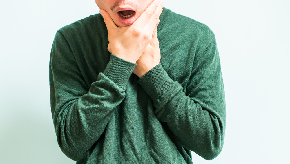 Man wearing a green shirt grasping his face due to TMJ pain