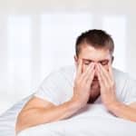 Tired young man laying in his bed with his eyes closed and his hands on his cheeks - sleep apnea and your health in Ottawa