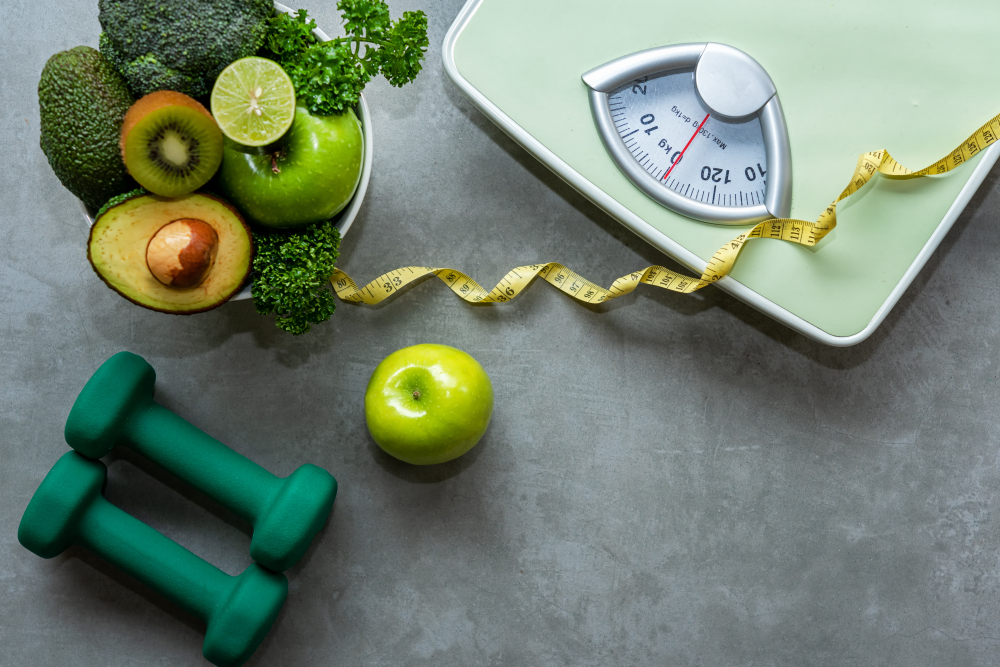 Green fruits and veggies in a bowl beside green weights and a green scale. All of these are tactics recommended to lose weight for sleep apnea.