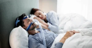 A man wearing an oxygen mask in bed with his partner.